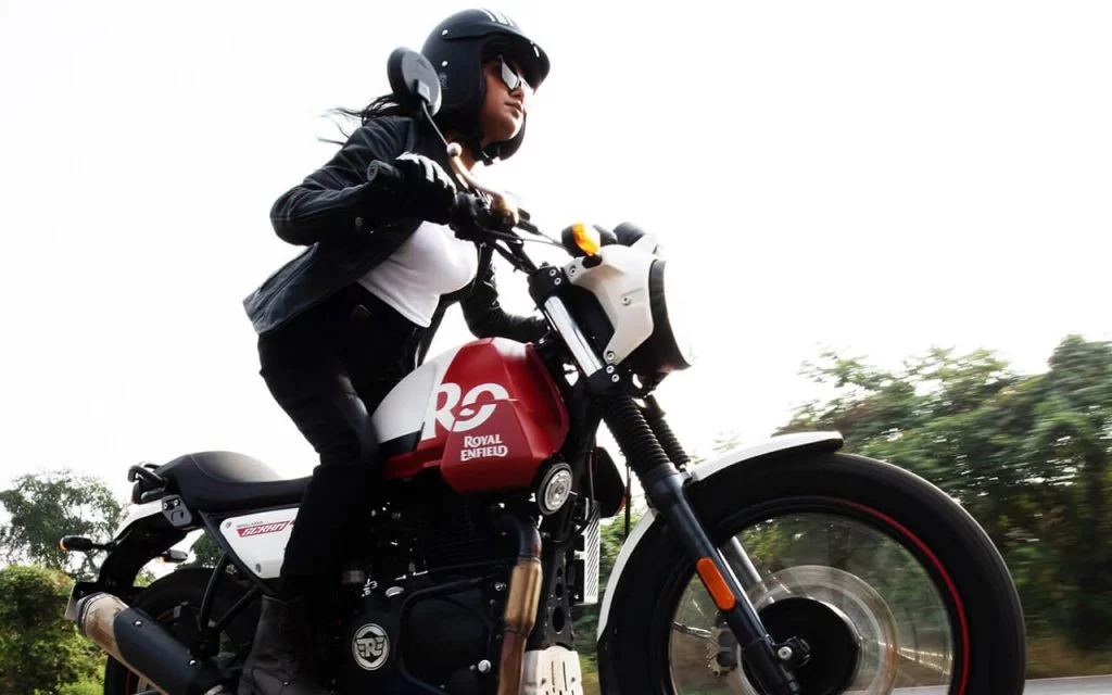 Actiefoto van onderkant genomen met vrouw staand op de voetsteunen van een Royal Enfield Scram 411