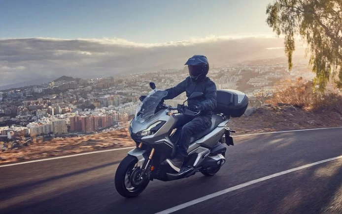 actiefoto van een motorrijder op een 2023-honda-adv-350-motorscooter met op de achtergrond de skyline van een stad