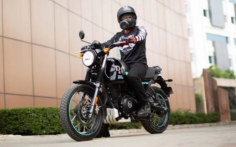 lifestyle foto van motorrijder op een scram 411 van royal enfield met gebouw op de achtergrond gevuld met zandkleurige muurpanelen