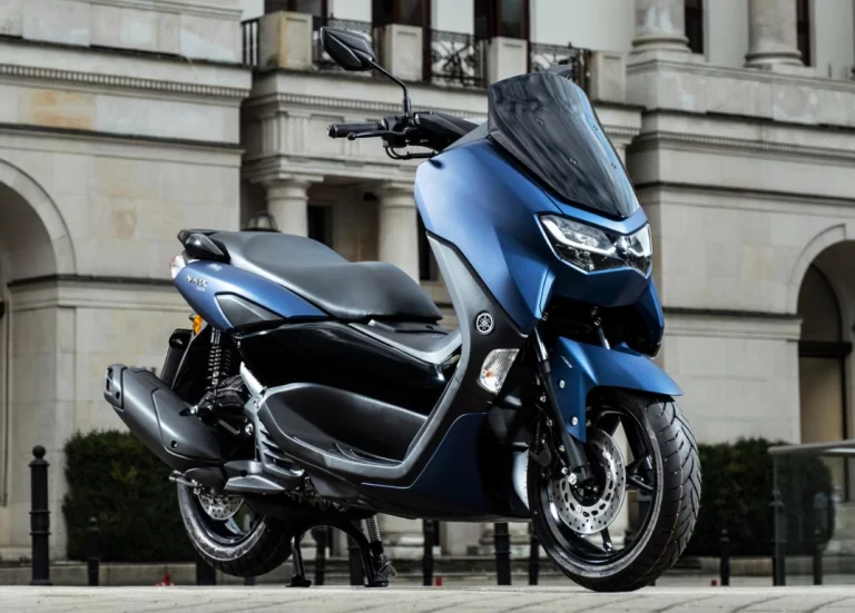 Lifestylefoto van blauwe 2023 Yamaha Nmax 155 in een stad met historisch gebouw op achtergond