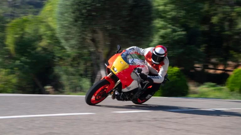 Motorrijder rijdt door een bocht op een rood met geel en witte Heritage gp motor