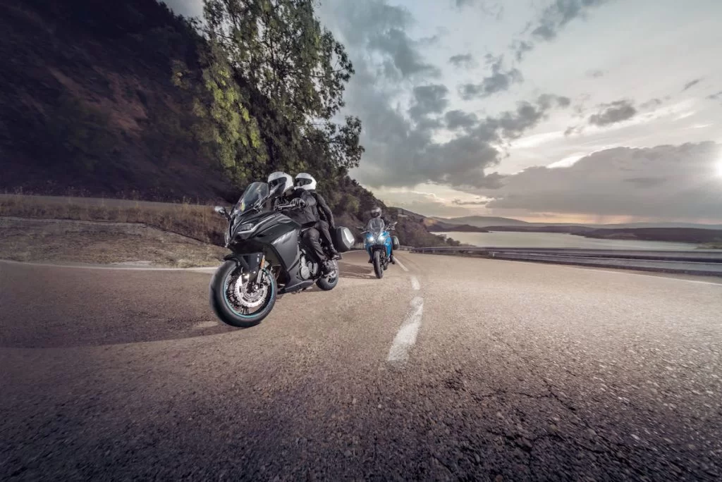 Actiefoto van twee motorrijders op een CF Moto 650 GT waarvan een met koffers uitgerust en de ander met passagier rijdend langs een heuvel