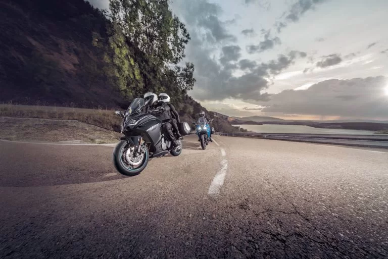 Actiefoto van twee motorrijders op een CF Moto 650 GT waarvan een met koffers uitgerust en de ander met passagier rijdend langs een heuvel