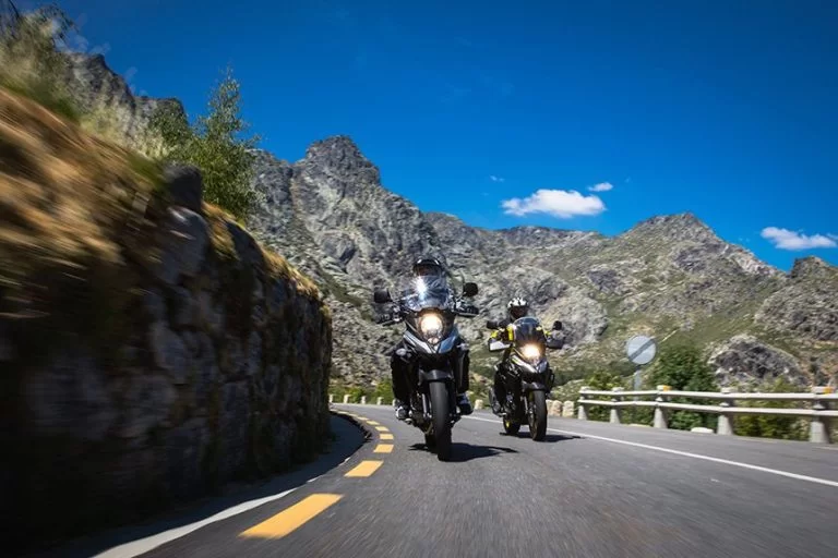 Actiefoto 2023 Suzuki V-Strom 650A van twee motorrijders die over een bergpas rijden met rotsachtige kliffen op de achtergrond