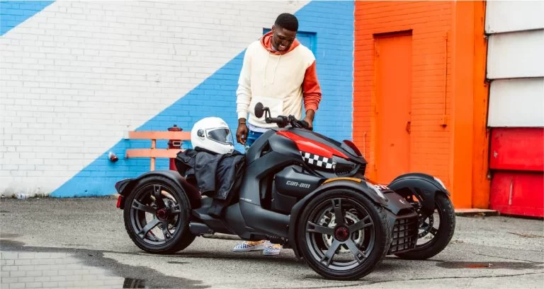 zwart met rode Can-Am Ryker 600 te zien vanuit het zijaanzicht met op de achtergrond een oranje met blauw en wit gebouw