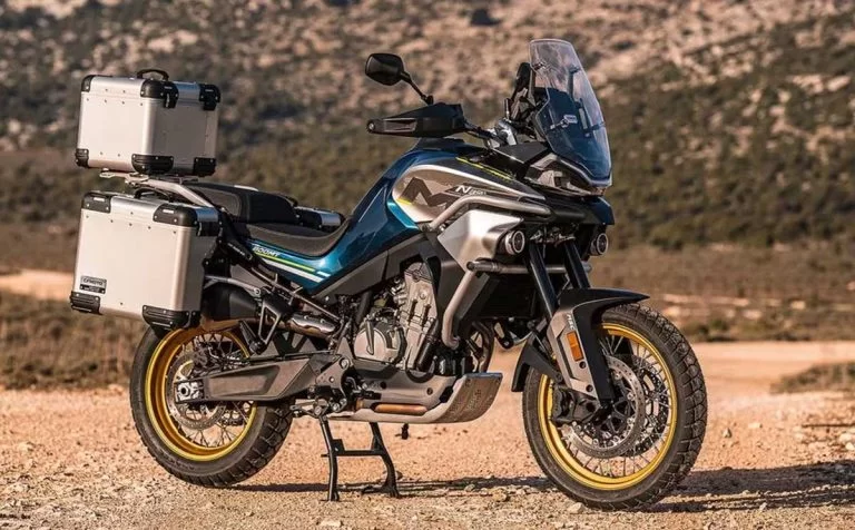 Lifestylefoto van CF Moto 800MT Touring blauw met koffers met ruig terrein op achtergrond