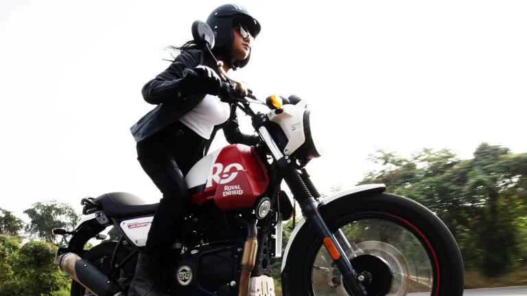 Vrouwelijk model op witrode Royal Enfield Scram 411. Aanzicht van schuinonder