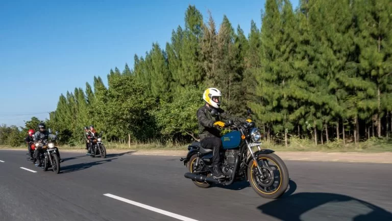 Drie Royal Enfield's Meteor 350 rijdend op een weg omgeven door groen bos met strak blauwe lucht