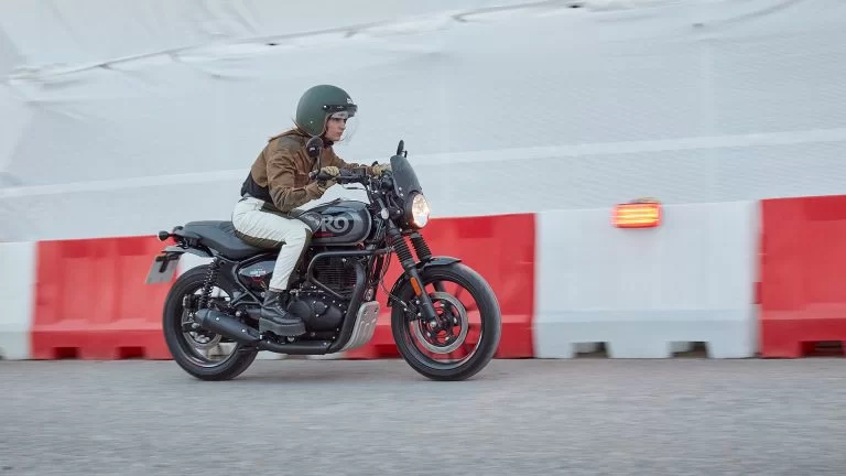 Actiefoto Royal Enfield Hunter 350 Rebel Black met motorrijder die langs roodwitte wegblokkades racet.