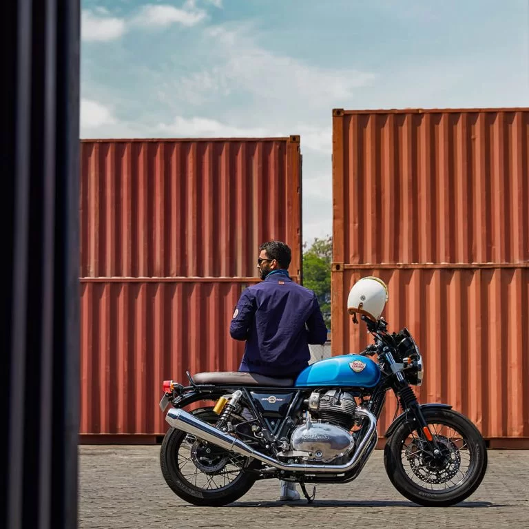 Model op een blauwe Royal Enfield's Interceptor 650 bij opslag voor containers in haven